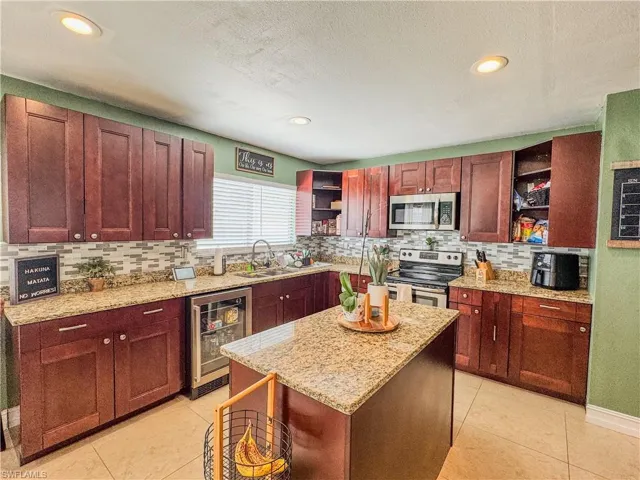 Kitchen with open shelves, stainless steel appliances, wine cooler, a sink, and decorative backsplash