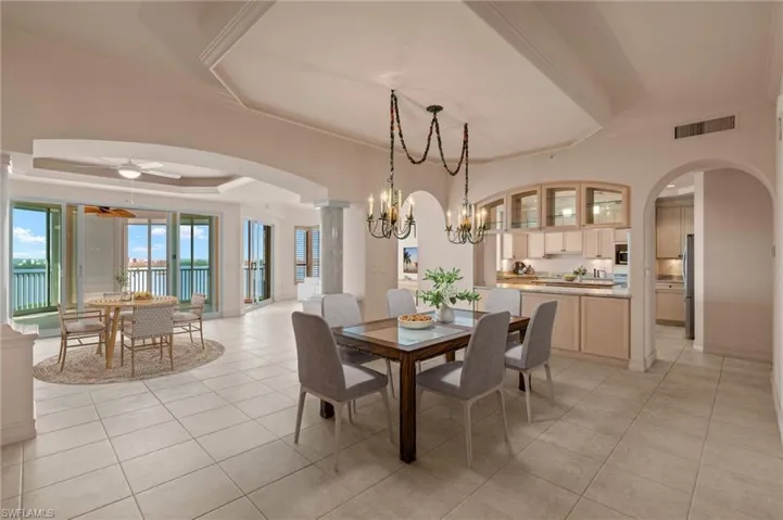 Virtually Staged. Dining area with arched walkways, light tile patterned floors, ceiling fan with notable chandelier, visible vents, and a tray ceiling