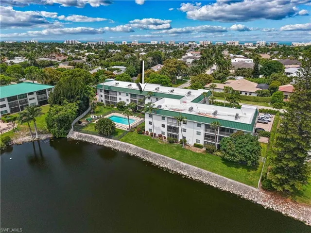 Waterfront condominium complex featuring a community pool, mature palm trees, and a manicured lawn