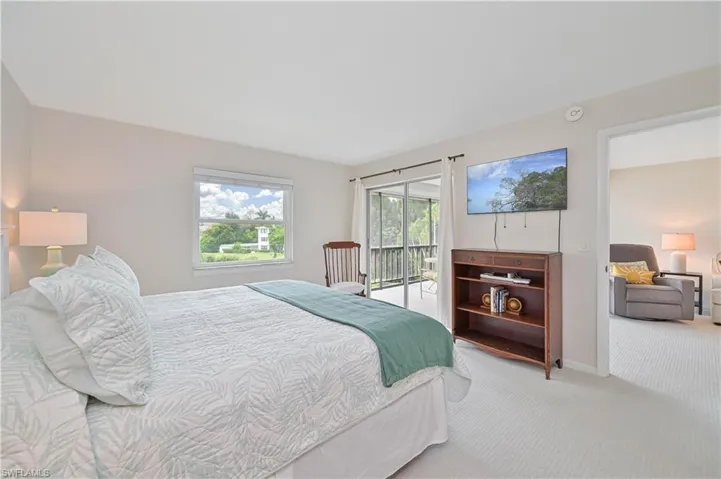 Bedroom featuring white textured carpeting, a window with outdoor scenery, and a sliding glass door opening to a screened balcony with railing