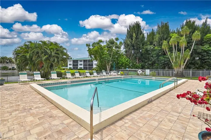 Outdoor swimming pool with integrated steps, surrounded by a paver patio and a metal fence