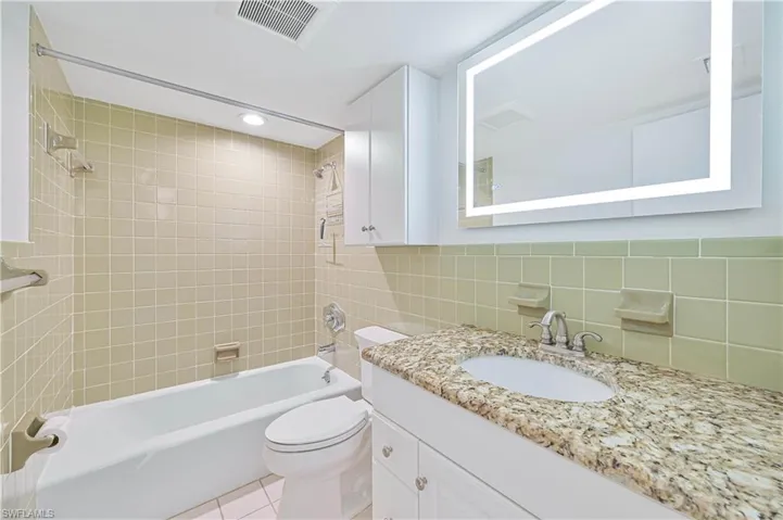 Bathroom featuring a white bathtub, light-colored square wall tiling, and a vanity with a granular countertop