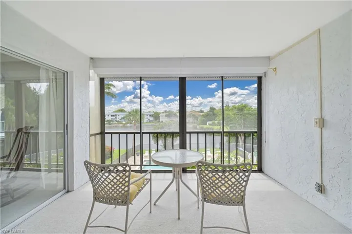 Screened balcony with waterway scenery, featuring a white textured ceiling, white textured walls, and a sliding glass door