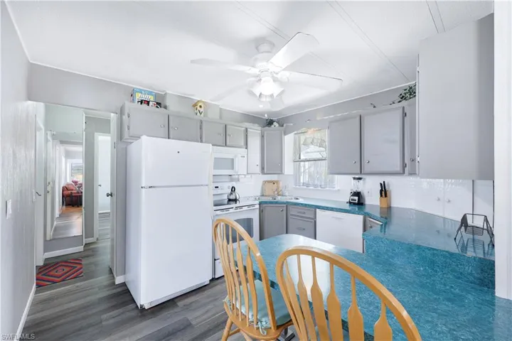 Kitchen with white appliances, gray cabinetry, dark wood-type flooring, and a ceiling fan