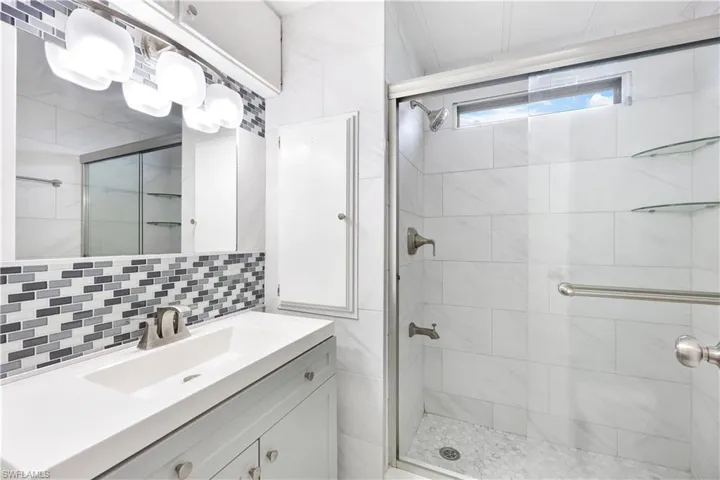 Bathroom with vanity, a stall shower, decorative backsplash, and tile walls