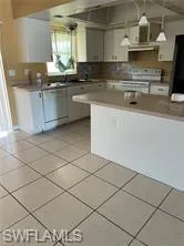 Kitchen featuring white cabinetry, white range with electric stovetop, hanging light fixtures, and light tile patterned floors