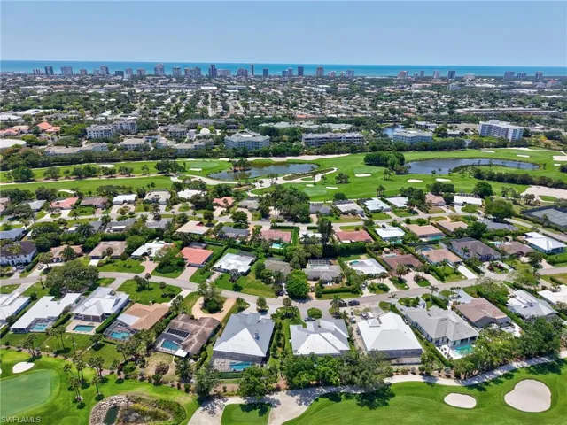 Aerial view of property's location featuring a golf club, a skyline view, a large body of water, and nearby suburban area