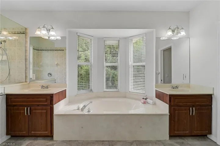 Bathroom featuring a chandelier, two vanities, a soaking bath, and tiled walk-in shower