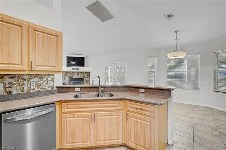 Kitchen featuring light brown cabinets, stainless steel dishwasher, a peninsula, and hanging light fixtures