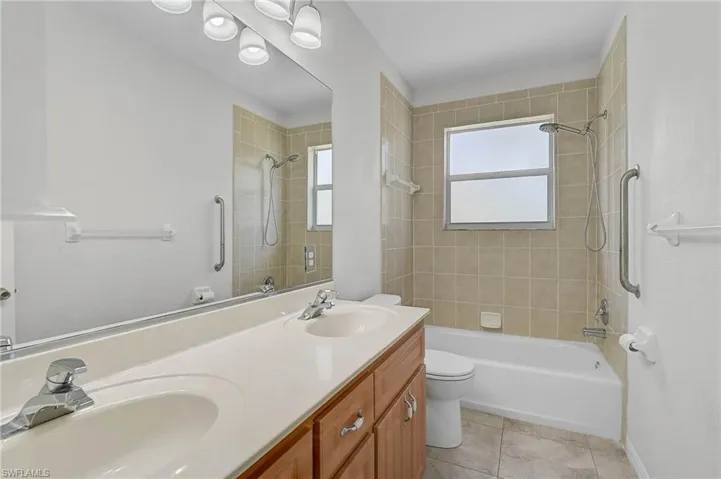 Bathroom with double vanity, washtub / shower combination, and light tile patterned floors