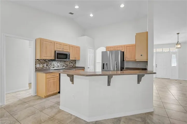 Kitchen featuring light brown cabinets, a breakfast bar area, high vaulted ceiling, appliances with stainless steel finishes, and a peninsula