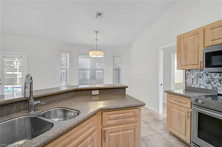 Kitchen featuring stainless steel appliances, light brown cabinets, decorative light fixtures, tasteful backsplash, and light tile patterned floors