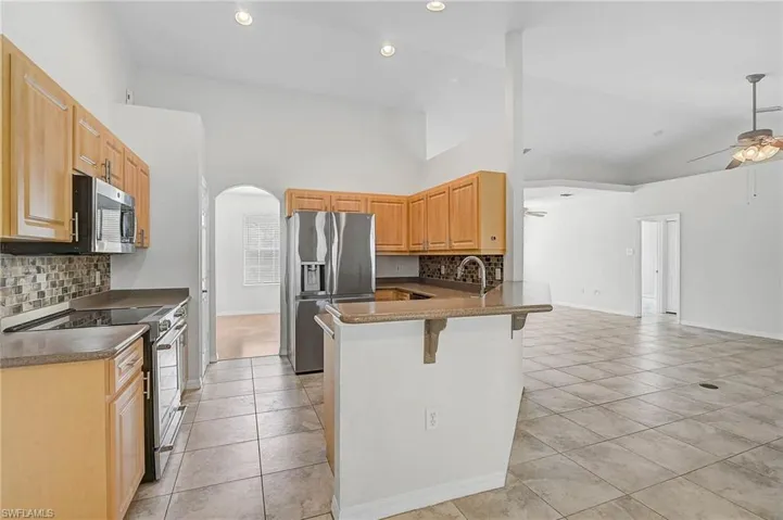 Kitchen with stainless steel appliances, arched walkways, a breakfast bar area, decorative backsplash, and high vaulted ceiling