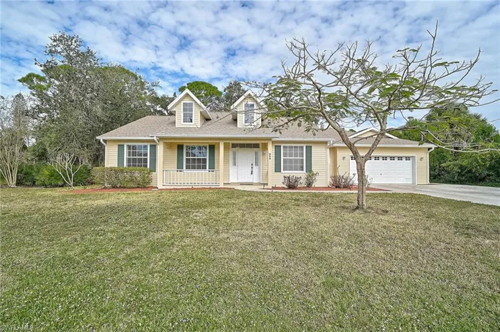View of front facade with a front yard, covered porch, driveway, roof with shingles, and an attached garage