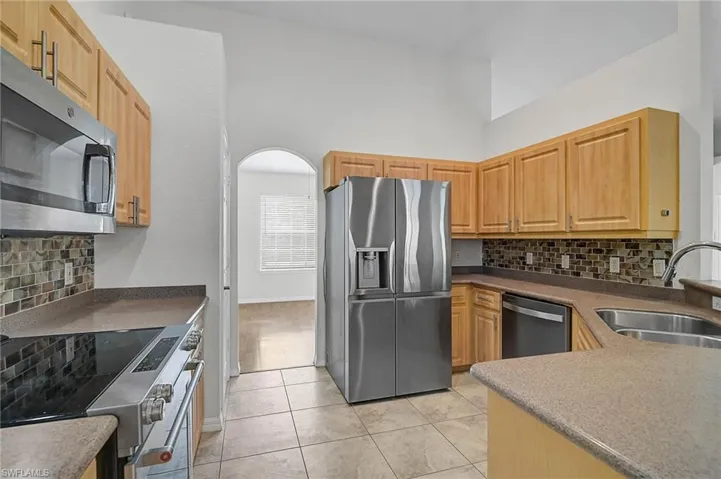Kitchen with tasteful backsplash, stainless steel appliances, arched walkways, light tile patterned floors, and high vaulted ceiling