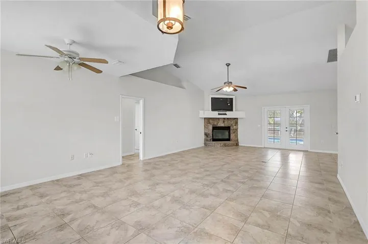 Unfurnished Bonus Room and Family room featuring french doors, ceiling fan, a fireplace, lofted ceiling, and light tile patterned floors