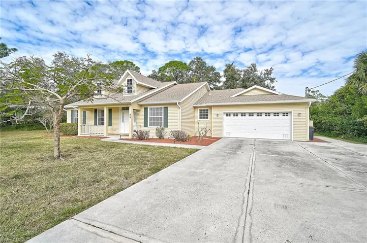 View of front facade with a front yard, extra wide concrete driveway, a shingled roof, an attached garage, and covered porch