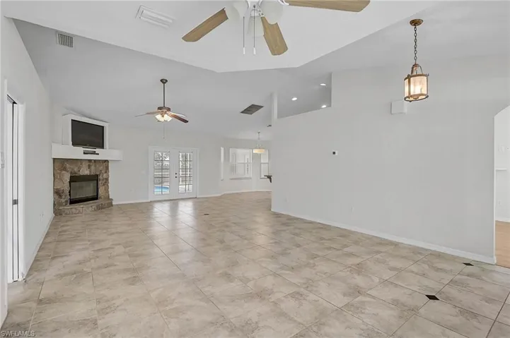Unfurnished living room featuring a stone fireplace, light tile patterned floors, a ceiling fan, and lofted ceiling