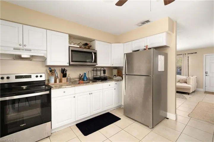 Kitchen with appliances with stainless steel finishes, under cabinet range hood, white cabinets, light tile patterned floors, and a ceiling fan