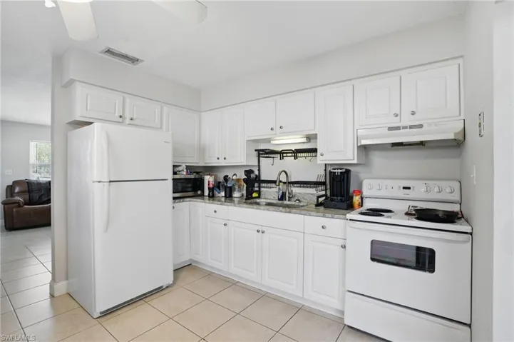 Kitchen with white appliances, under cabinet range hood, a sink, light tile patterned flooring, and white cabinetry