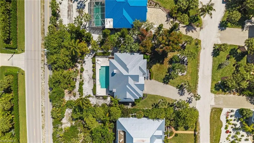 Aerial view of the property featuring a gray roof, an exterior pool, and surrounding green landscaping