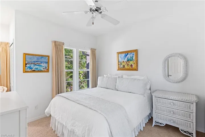 This room features a white ceiling fan, windows with curtains providing natural light, and carpeted flooring