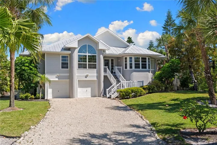 The property features a light gray exterior with a white metal roof, and a gravel driveway leading to two garage doors