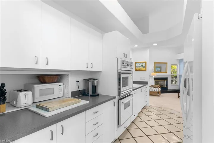 The kitchen features white cabinetry, integrated double ovens, and a countertop with a microwave and toaster