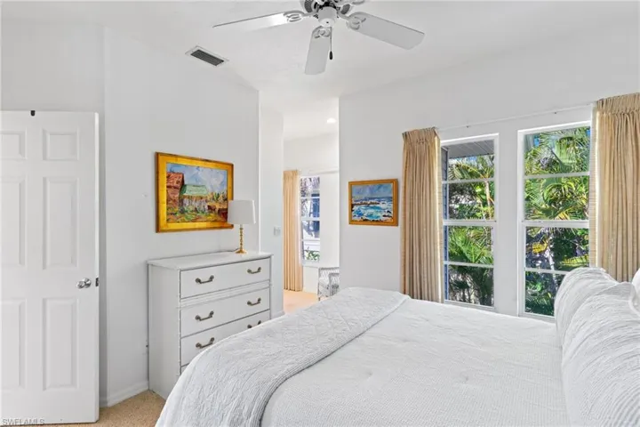 The room features windows with exterior views of lush greenery, a white ceiling fan, and light-colored carpeting