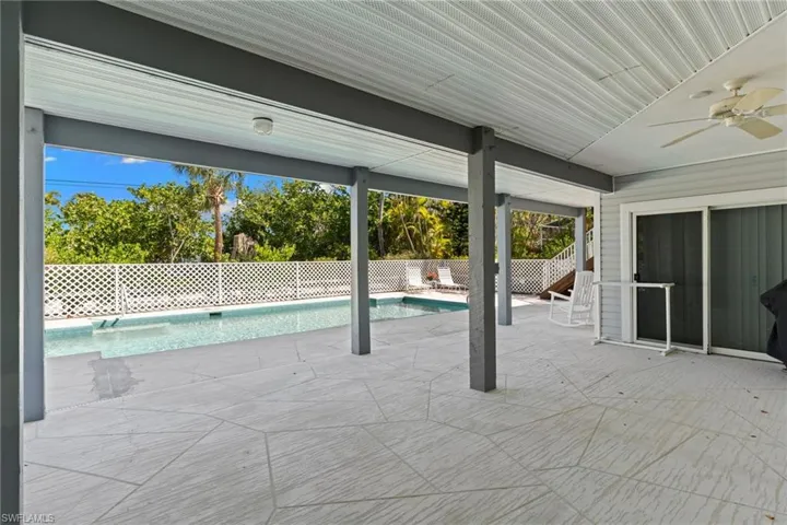Expansive covered patio with a textured flooring, offering direct views of the swimming pool and surrounding greenery