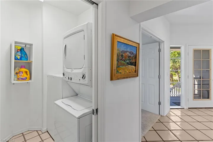 This area of the property features a stacked washer and dryer unit, a wall-mounted storage shelf, and tile flooring
