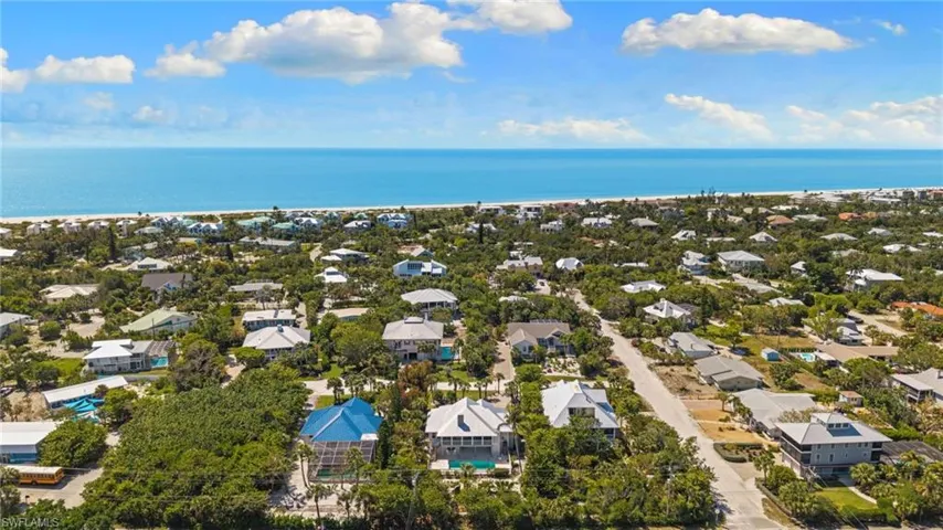 Aerial view of the coastal community, featuring a variety of homes surrounded by lush trees, with the ocean and beach visible in the background