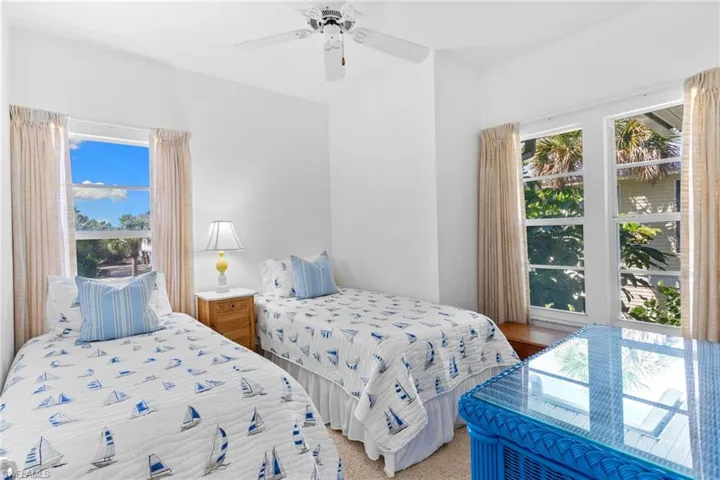 Bright room featuring two windows with views of greenery and the sky, a ceiling fan, and white walls