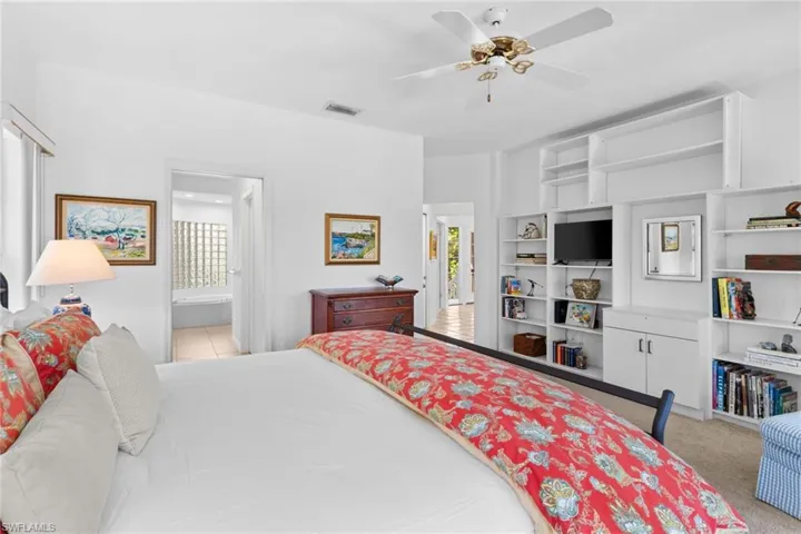 Bedroom featuring a ceiling fan, built-in shelving, and a view into an adjoining space with tiled flooring and glass block windows