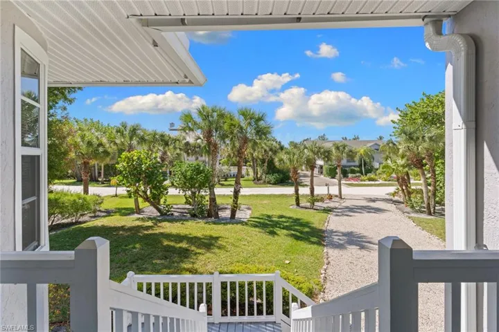 The property features a well-maintained lawn and mature palm trees, with a gravel driveway leading to the street