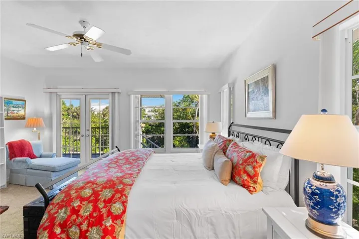 This bright room features a ceiling fan, a set of French doors leading to a balcony, and abundant natural light from multiple windows