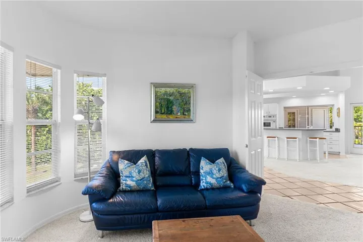 Living area featuring bright white walls, carpeted flooring, and a series of windows providing natural light and exterior views