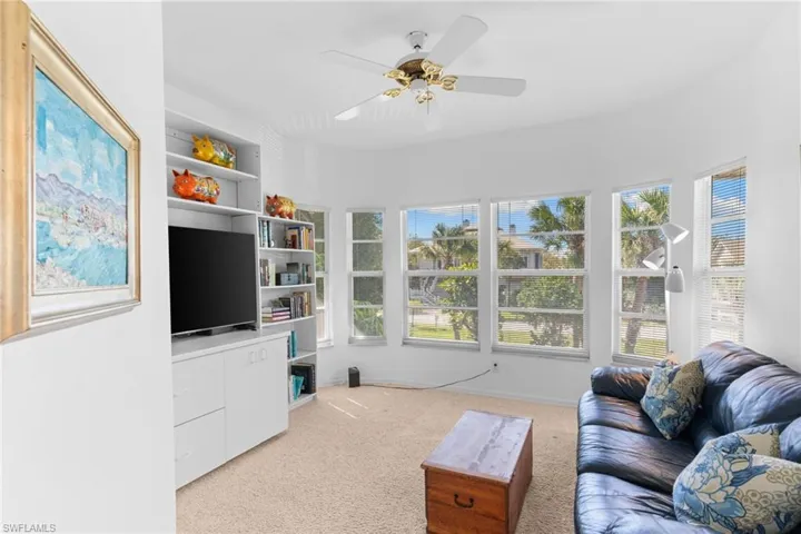 This bright living space features a ceiling fan, plush carpeting, and a built-in media center with shelving