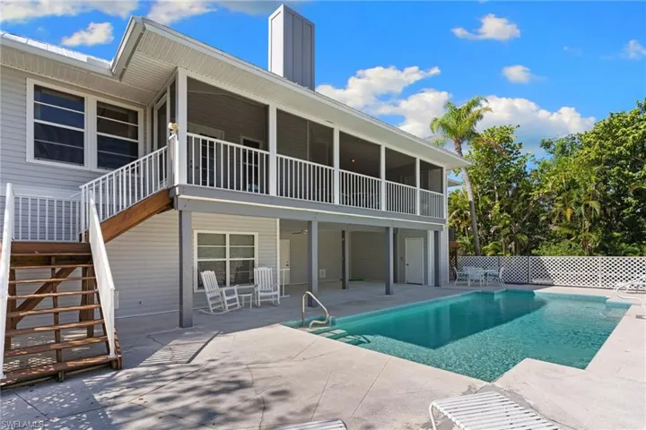 The property features a private swimming pool with concrete decking, surrounded by lush tropical trees and a white lattice fence