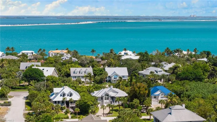 An aerial view showcasing properties nestled amongst lush green foliage, with a vibrant blue waterway and a distant landmass visible under a clear sky
