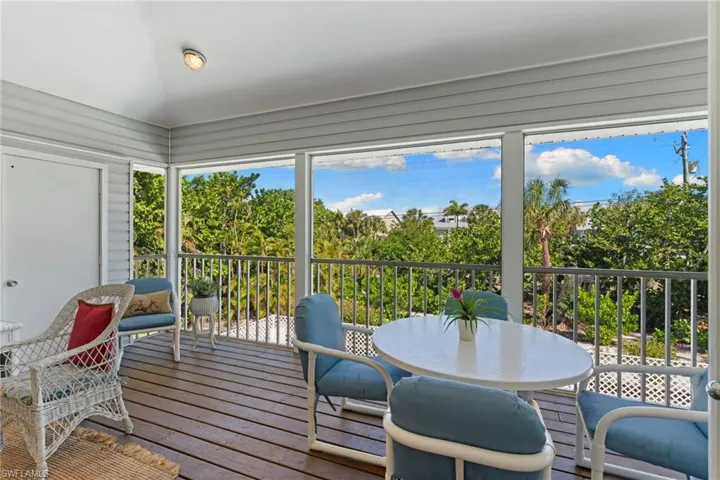 The property features a screened-in porch with a slatted wood floor and a white railing, offering views of abundant green foliage and the blue sky
