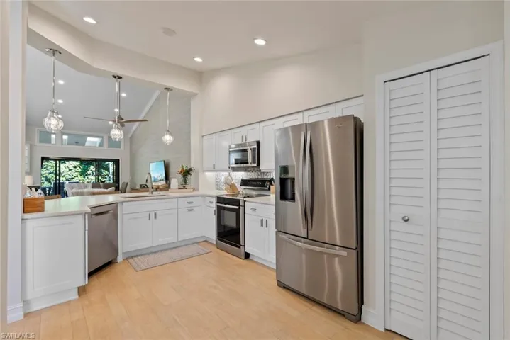 Kitchen with decorative light fixtures, high vaulted ceiling, white cabinets, stainless steel appliances, and backsplash