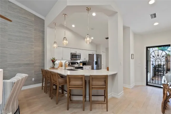 Kitchen with white cabinetry, stainless steel appliances, kitchen peninsula, and hanging light fixtures