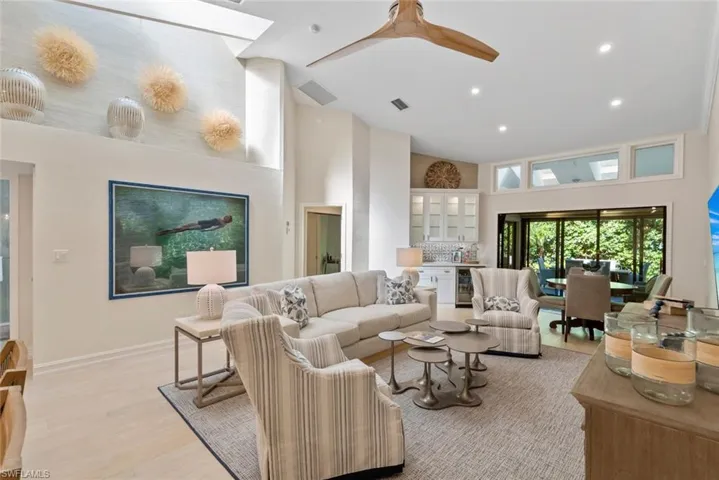 Living room with a high ceiling, ceiling fan, wine cooler, and light wood-type flooring
