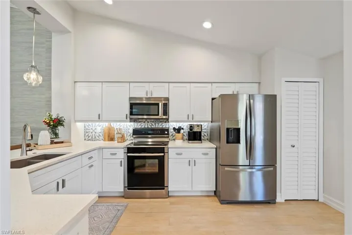 Kitchen with sink, white cabinetry, stainless steel appliances, decorative backsplash, and decorative light fixtures
