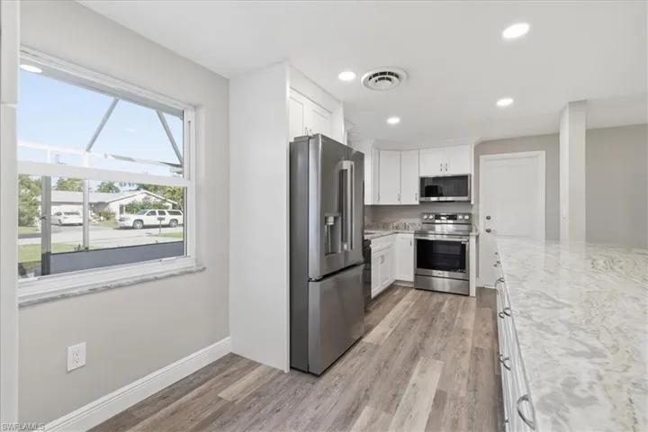 Kitchen with stainless steel appliances, white cabinets, light wood-type flooring, light stone counters, and recessed lighting