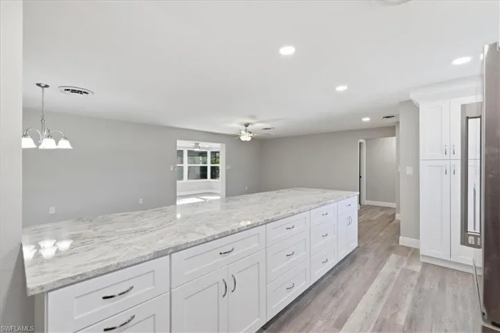 Kitchen featuring white cabinetry, light wood-style flooring, light stone counters, a ceiling fan, and hanging lights