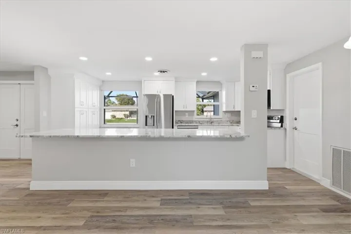 Kitchen island featuring light stone counters, stainless steel appliances, white cabinets, a peninsula, and light wood finished floors