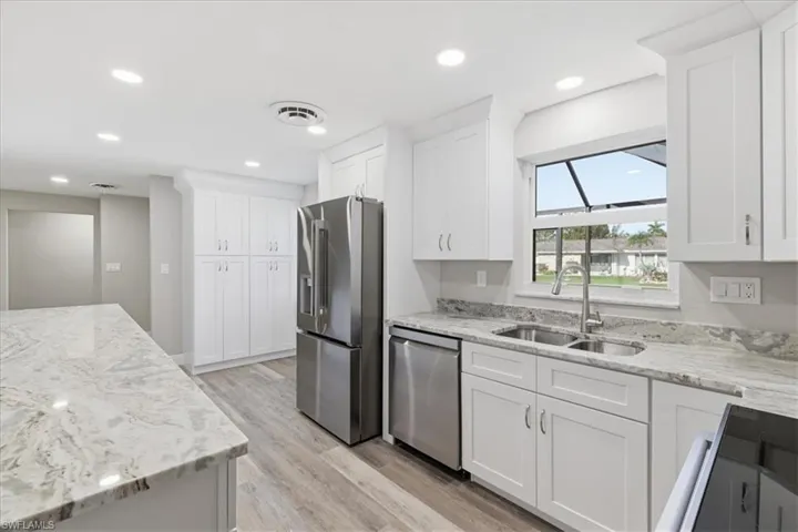 Kitchen featuring stainless steel appliances, light stone countertops, white cabinetry, light wood finished floors, and recessed lighting