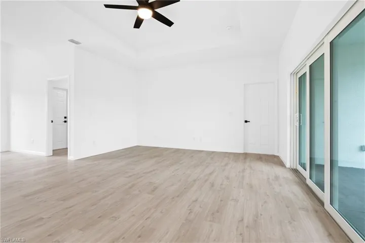Spare room featuring light hardwood / wood-style floors, ceiling fan, and a tray ceiling